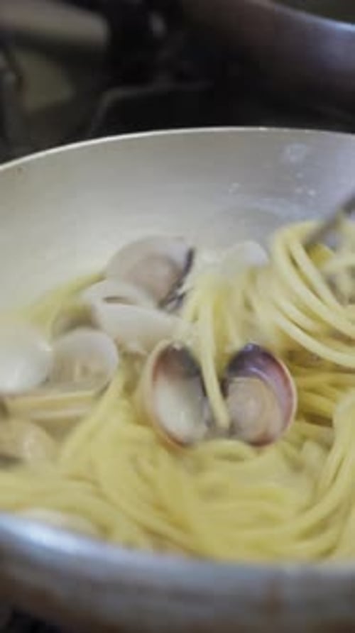 Cuisiner des pâtes spaghettis avec des palourdes dans la poêle d'un restaurant