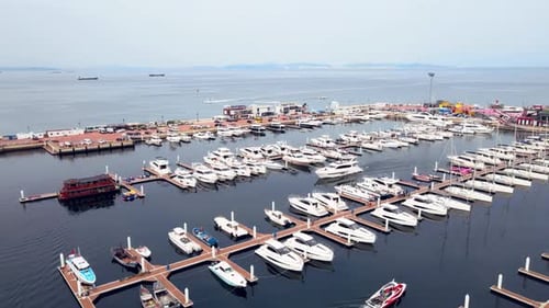 Aerial view of a marina at dusk with multiple luxury boats and yachts catamarans docked moored to pi