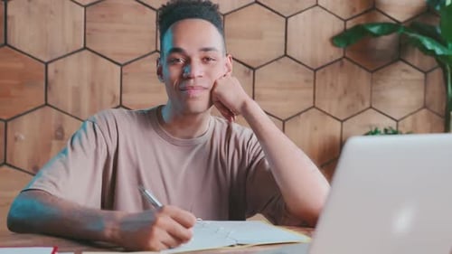 Young Man Writing at Desk with Laptop