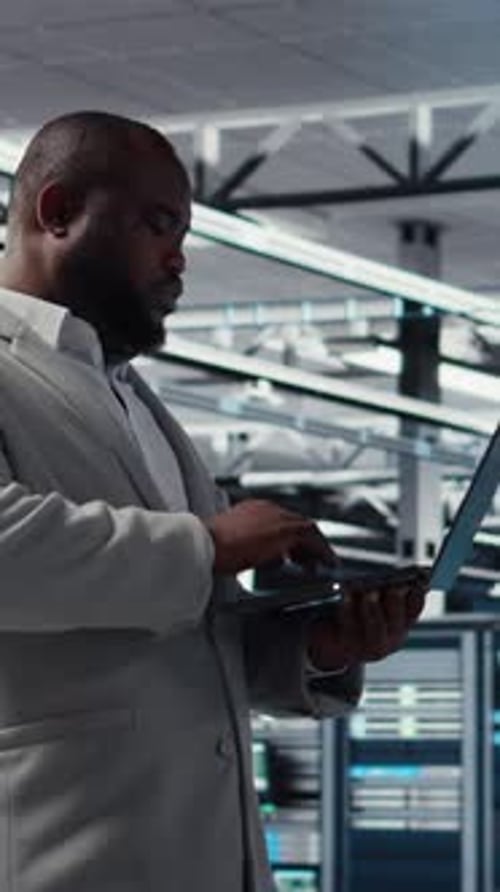 Man in Suit Works on Laptop in Server Room