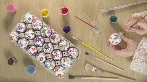 Female hands painting with paints and brush on an Easter eggs