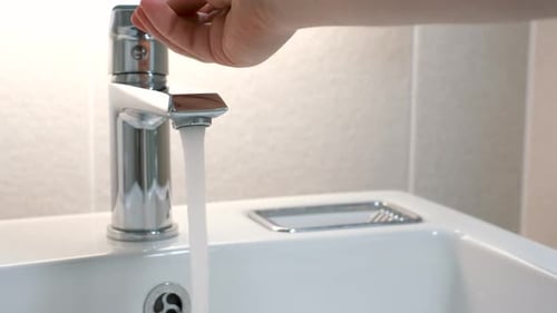 Weibliche Hand dreht das Wasser im Wasserhahn im Badezimmer auf.