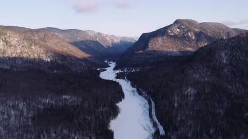 Epic backwards moving aerial wide landscape shot of snowy river flowing through fjord into winter bo