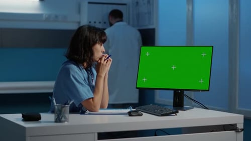Asistente médico de pie en el escritorio mirando la computadora con pantalla verde