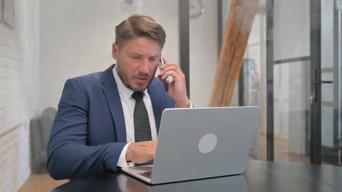 Businessman Talking on Phone While Working on Laptop