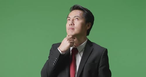 Ein asiatischer Geschäftsmann, der über etwas nachdenkt und sich auf dem Greenscreen im Studio umschaut