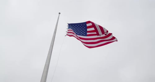 Drapeau américain en berne, agitant doucement sur un ciel dégagé. La scène reflète une célébration solennelle et