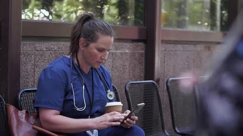 Nurse Texting On Phone In Covered Bus Stop