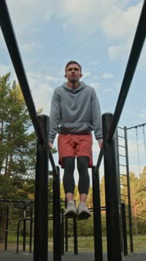 Männlicher Athlet beim L-Sit auf parallelen Dip-Bars im Freien