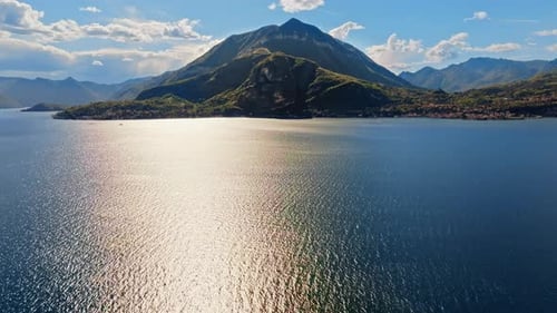 Aerial drone view of Lake Como, Italy surrounded by mountains with clouds on a blue sky