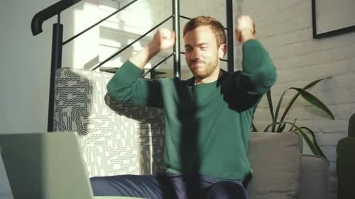 Excited Man Cheering While Using Laptop At Home