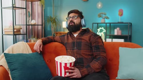 Man Watches TV and Eats Popcorn on Couch