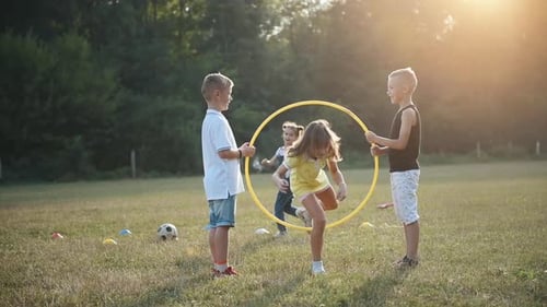 Male kids holding fitness circle in hands and girls having fun by jumping through it