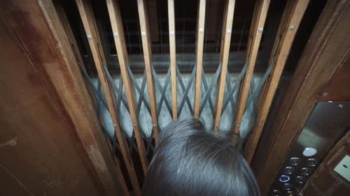Una persona que mira a través de la puerta de madera y acero de un ascensor antiguo mientras baja