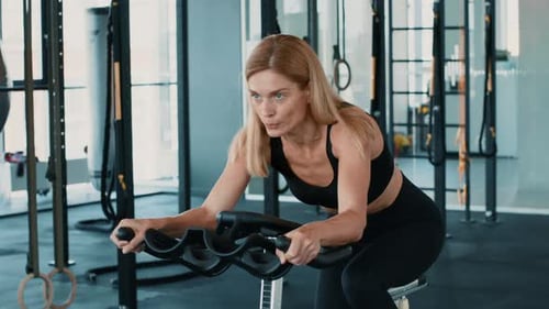 Woman Exercising on a Bike in a Modern Gym With Fitness Equipment Around Her