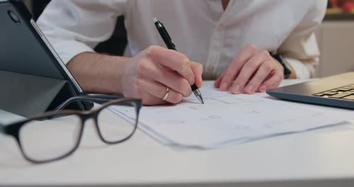 De cerca. Hombre con ropa elegante sentado en la mesa de la cocina y trabajando con documentos importantes