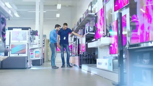 In the Electronics Store Professional Consultant Shows Latest 4K UHD TV's to a Young Man, They Talk