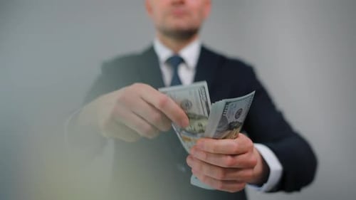 Homem vestido formalmente joga notas de dólar americano em direção à câmera