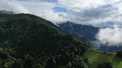 A mountainous landscape with trees and clouds Some of the mountains are covered in green vegetation