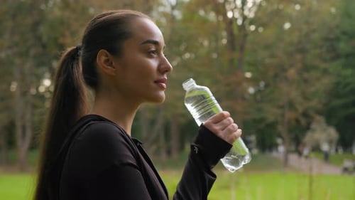 Young Woman Drinks Water Bottle in Park