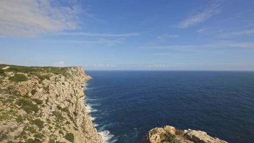 A Rocky Cliff Overlooks the Ocean with a Lighthouse in the Distance