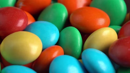 Sweet dragees in colored glaze are rotating background macro side light. Delicious sweets