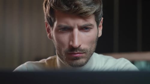 Porträt eines jungen Designers, der an einem Laptop arbeitet, fokussierter Mann schaut in die Kamera und lächelt gut