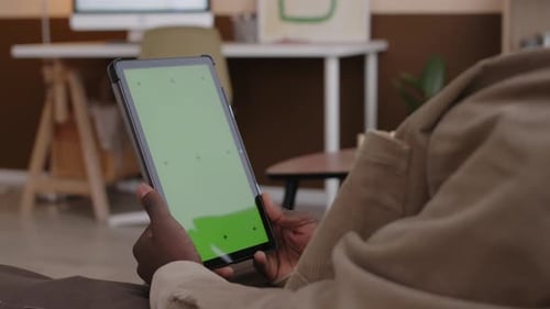 Man Looking at Digital Tablet with Green Screen at Home