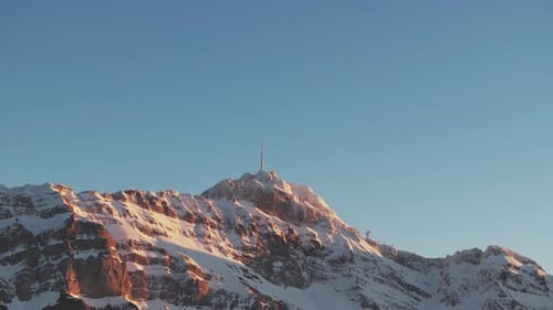 Mesmerizing drone footage displaying the silhouette of a snowy mountain range during sunrise.