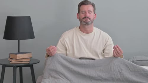 Homme d'âge moyen faisant du yoga assis sur son lit