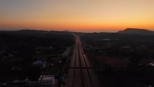 Lange Straße, die sich unter dem frühen Morgenhimmel mit warmem orangefarbenem Schein zum Horizont erstreckt, Autos bewegen sich langsam