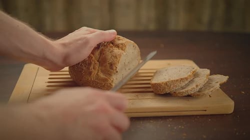 Hands Slicing Fresh Bread Loaf on Cutting Board