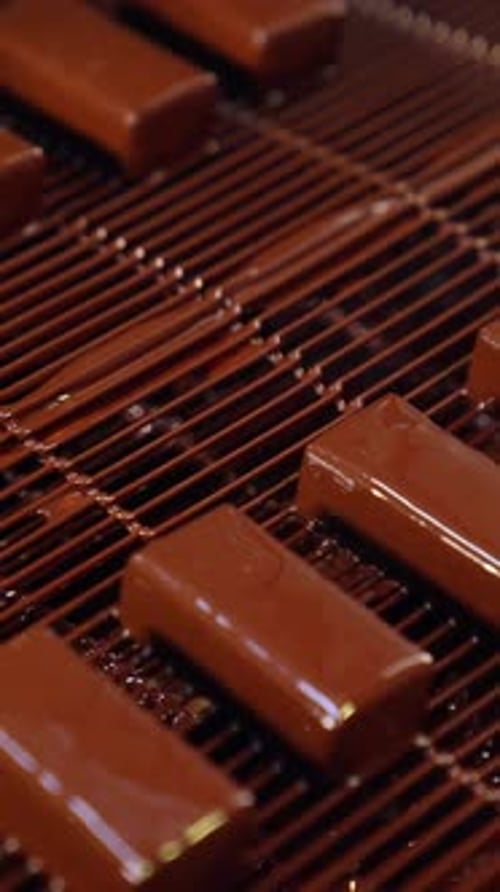 Deliciosos dulces recién cubiertos con glaseado de chocolate negro. Transportador de rejilla lleno de chocolate