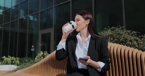 Woman Drinking Coffee Using Phone Outside Office Building