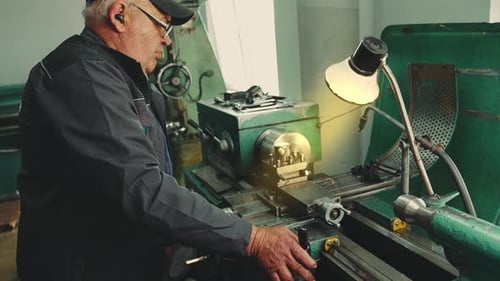 An elderly senior turner mechanic works at a vintage old Soviet lathe