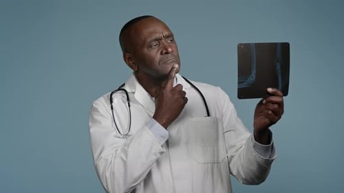 Pensive Thoughtful African American Man Doctor Ethnic Male Radiologist Surgeon in Studio Blue
