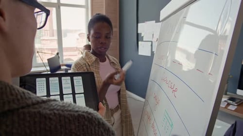 Black Female UX Designer Presenting Workflow Plan to Colleague at Office