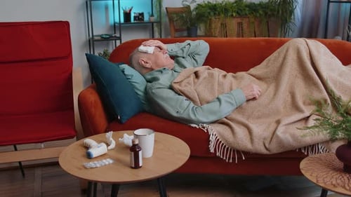 Un homme âgé malade souffrant d'allergie au froid, allongé sur le canapé de la maison, éternuant, essuie de la morve dans une serviette