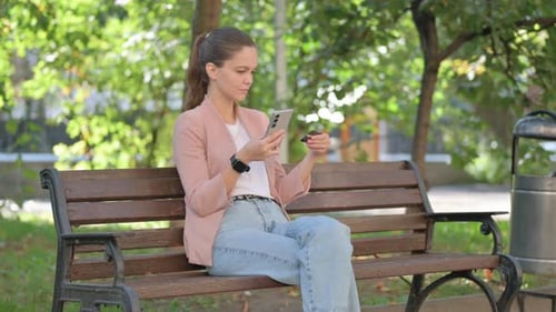 Young Woman Shopping Online with Credit Card and Phone in Park