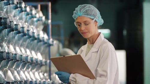 Une travailleuse inspecte la qualité de l'eau et des bouteilles dans une usine de production d'eau potable