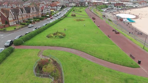 An aerial photo of a park in a seaside town. The park is filled with green grass, trees, and bushes.