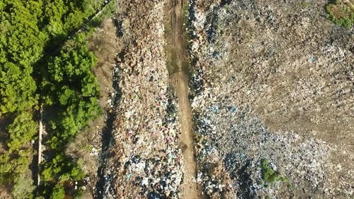 Aerial top view of a road leading through huge landfill pile of dump and trash within mangrove trees