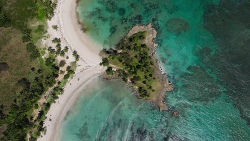 Ocean waves roll into sandy bays over coral reef with tropical palm trees and white sandy beach, dro