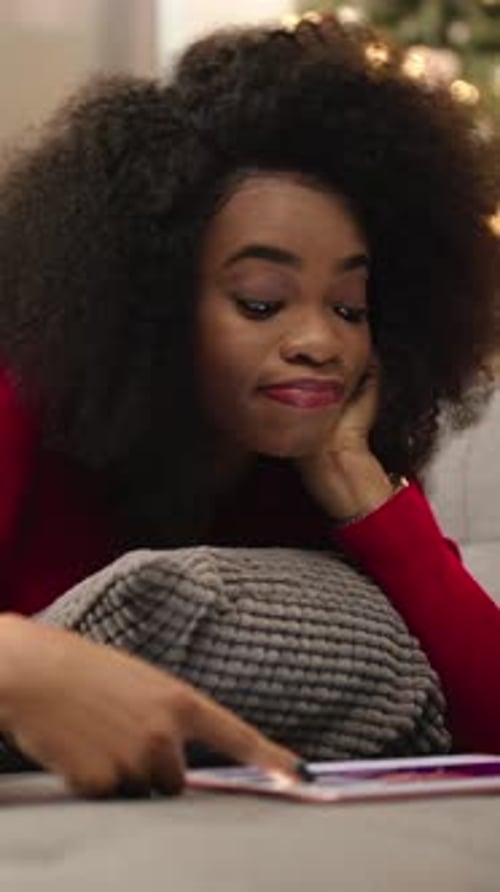 Attractive Girl with Curly Hair Laying on Couch and Watching Video on Tablet in Evening Young Tired
