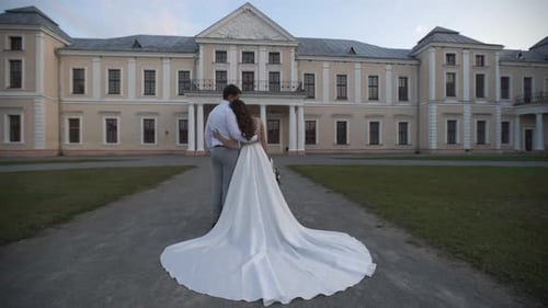 Happy wedding couple standing together at sunset on the background of a beautiful building