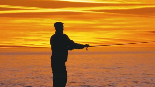 Silhouette eines Fischers mit einer Angelrute bei Sonnenuntergang über dem Meer