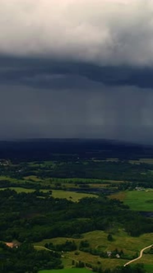 Aerial view of approaching storm clouds over lush green countryside, vertical shot