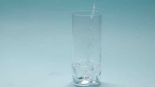 Studio Shoot of Water Pouring Into Transparent Glass on Blue Background Slow Motion Video Close Up