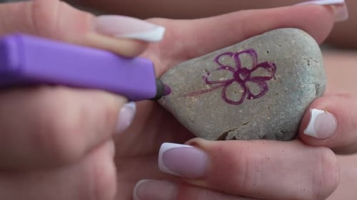 Malstein, Blume, Frau, die Kunst mit violettem Marker auf Strandkiesel kreiert