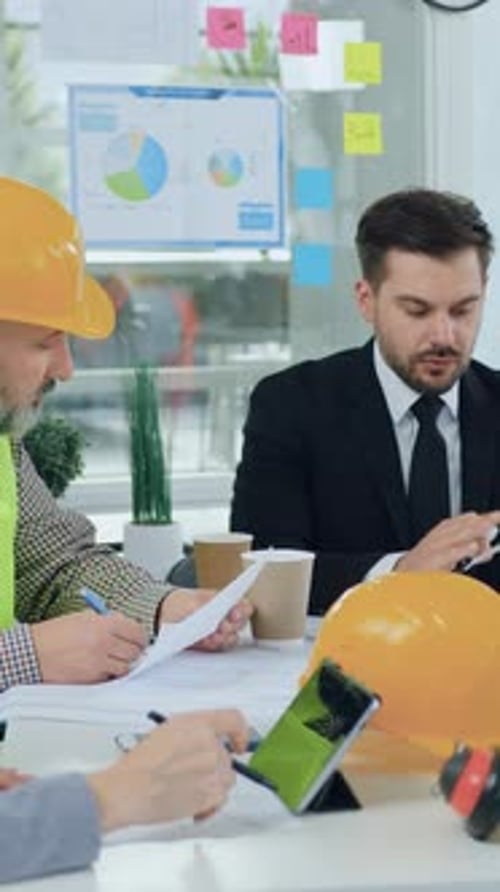 Attractive Confident Experienced Bearded Engineer in Light Green Vest and Hardhat Discussing with